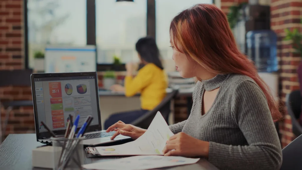 Asian woman working on e commerce growth in business office, looking at financial graphics on papers. Accountant analyzing sa
