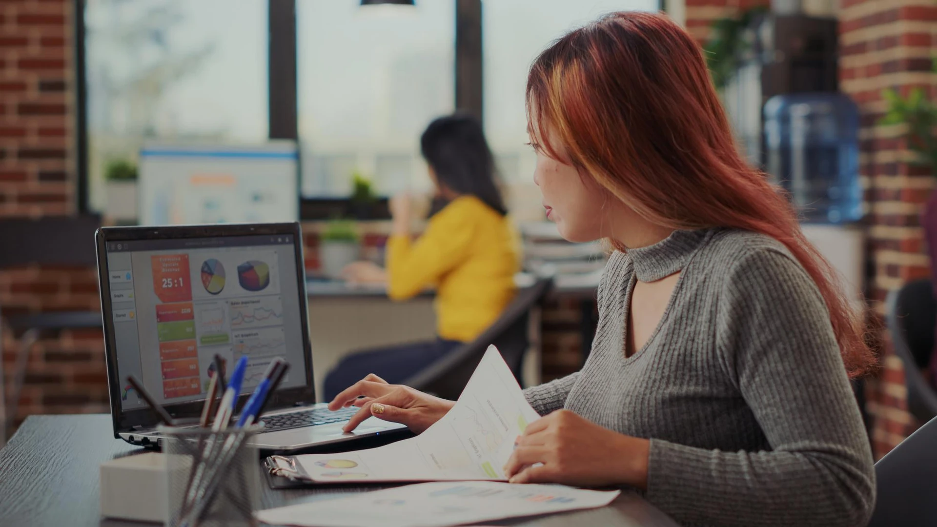 Asian woman working on e commerce growth in business office, looking at financial graphics on papers. Accountant analyzing sa